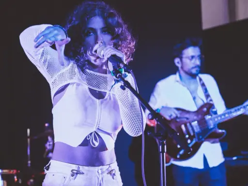 Une chanteuse au look audacieux, micro en main, semble exprimer son dédain pour une chanson nulle. Un guitariste l'accompagne sur scène.