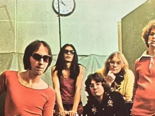 Cinq membres des Flamin' Groovies posent dans un studio. L'un d'eux porte des lunettes de soleil et un t-shirt orange.