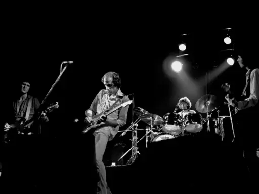 Quatre musiciens sur scène, guitares et batterie. Un aperçu de la **dire straits discography** en live.
