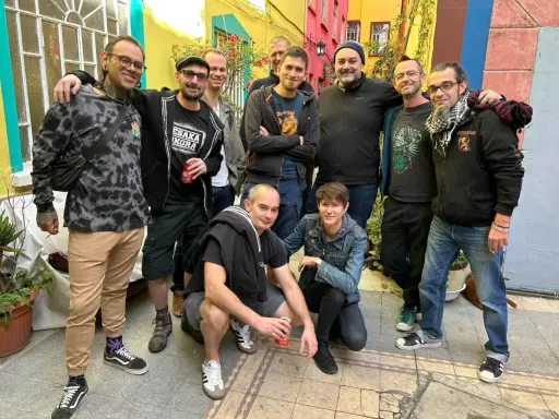 Un groupe d'amis, dont certains portent des t-shirts avec des motifs ska p, pose joyeusement dans une ruelle colorée.