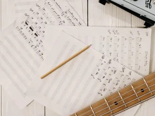 Feuilles de musique manuscrites, un crayon et une guitare. Le matériel parfait pour trouver l'inspiration pour écrire une chanson.