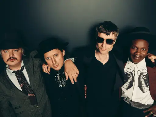 Quatre hommes stylés, comme des libertins modernes, posent ensemble. L'un porte un chapeau et une veste rayée, un autre un chapeau noir et une chemise à jabot. Le troisième, lunettes de soleil, est en noir. Le dernier, chapeau et veste bordeaux, arbore...