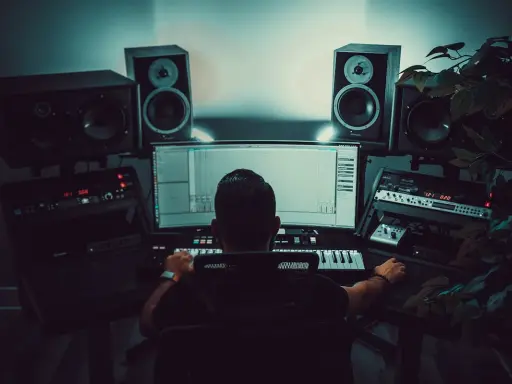 Un producteur de musique travaille dans son studio, entouré d'enceintes et d'équipements audio. Il manipule une interface logicielle, peut-être pour un projet avec un isrc code.