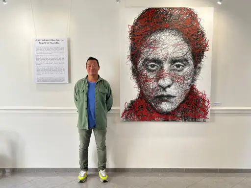 Un homme pose devant un portrait abstrait de Jean Cocteau, une œuvre de Hom Nguyen. La liste nom d'artiste est visible sur le mur.