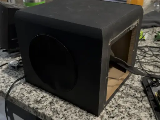 Un caisson de basse noir ouvert sur une table. Pour savoir si un caisson de basse fonctionne, vérifiez les connexions et le circuit imprimé.