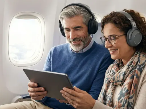 Couple souriant dans un avion, partageant une tablette et des écouteurs. Apprenez comment connecter deux appareils Bluetooth en même temps pour un voyage agréable.