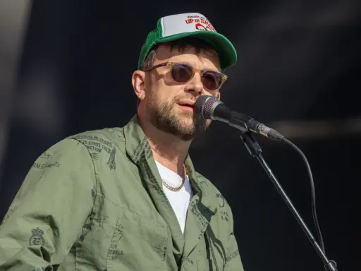 Damon Albarn, chanteur du groupe Gorillaz, porte une casquette et une veste verte ornée de motifs.
