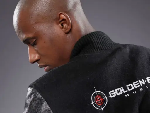 Un homme chauve porte une veste noire avec le logo "Golden Eye Music". Il est prêt à faire le buzz avec sa musique.