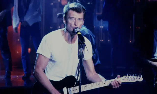 Johnny Hallyday chante en live, guitare à la main. On se demande combien gagne un musicien de Johnny Hallyday pour une telle performance.