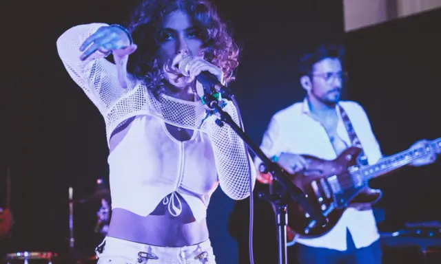 Une chanteuse au look audacieux, micro en main, semble exprimer son dédain pour une chanson nulle. Un guitariste l'accompagne sur scène.