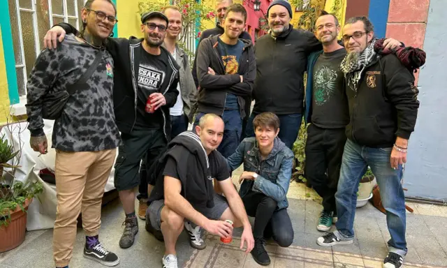 Un groupe d'amis, dont certains portent des t-shirts avec des motifs ska p, pose joyeusement dans une ruelle colorée.