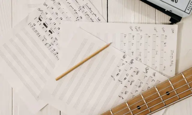 Feuilles de musique manuscrites, un crayon et une guitare. Le matériel parfait pour trouver l'inspiration pour écrire une chanson.