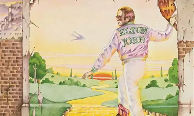 Elton John, sur la couverture du meilleur album Elton John, marche sur la route de briques jaunes vers un paysage idyllique.