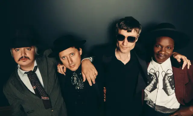 Quatre hommes stylés, comme des libertins modernes, posent ensemble. L'un porte un chapeau et une veste rayée, un autre un chapeau noir et une chemise à jabot. Le troisième, lunettes de soleil, est en noir. Le dernier, chapeau et veste bordeaux, arbore...