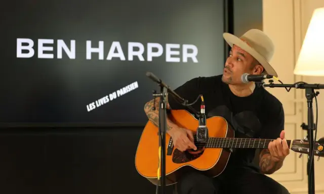 Ben Harper, chapeau sur la tête, joue de la guitare devant un écran affichant son nom et "Les Vies du Parisien".