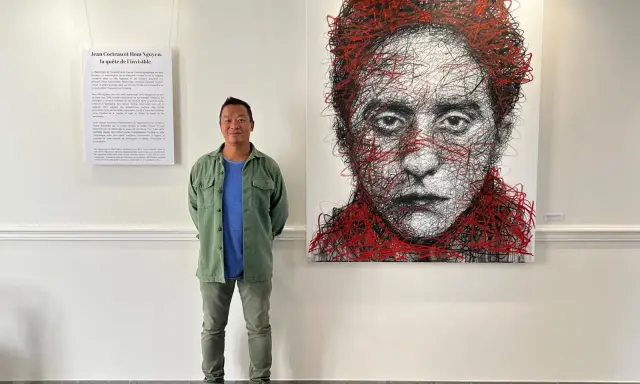 Un homme pose devant un portrait abstrait de Jean Cocteau, une œuvre de Hom Nguyen. La liste nom d'artiste est visible sur le mur.