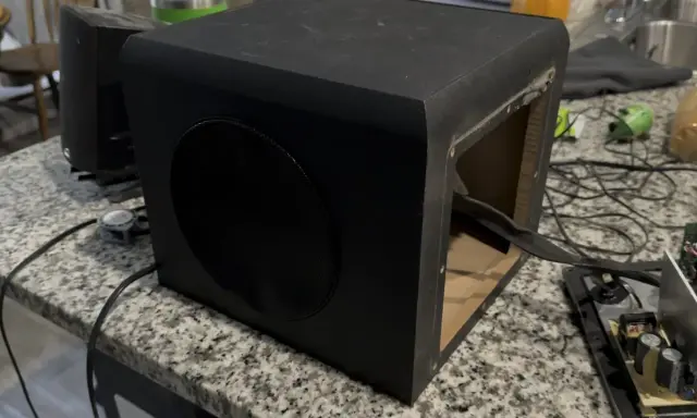 Un caisson de basse noir ouvert sur une table. Pour savoir si un caisson de basse fonctionne, vérifiez les connexions et le circuit imprimé.