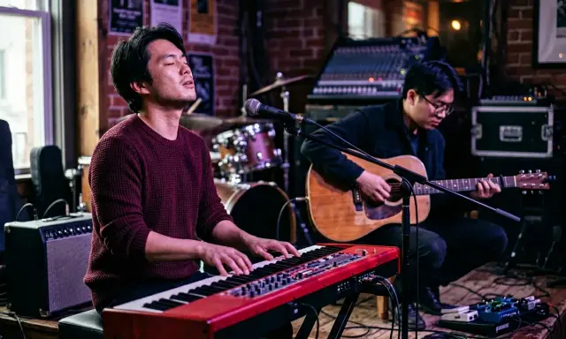 Deux musiciens jouent sur scène. L'un au piano rouge, l'autre à la guitare acoustique. Parfait pour un blog musique.