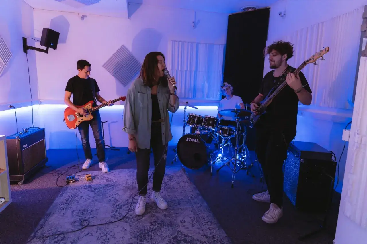 Un groupe de musique r&eacute;p&egrave;te dans un studio. La chanteuse est au micro, le guitariste joue, le bassiste est pr&ecirc;t &agrave; rejoindre le groupe.