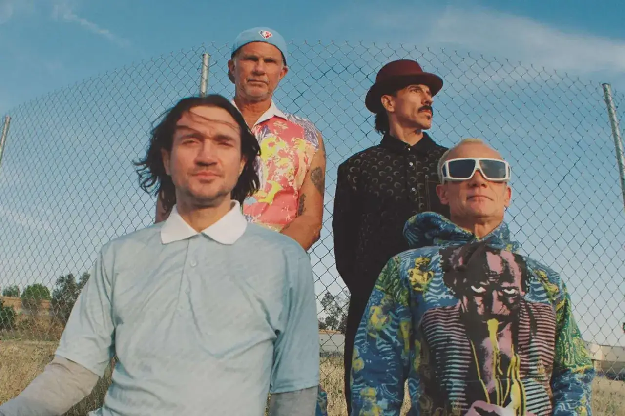 Les membres des Red Hot Chili Peppers posent devant une cl&ocirc;ture. Flea porte des lunettes de soleil et un sweat &agrave; capuche color&eacute;.