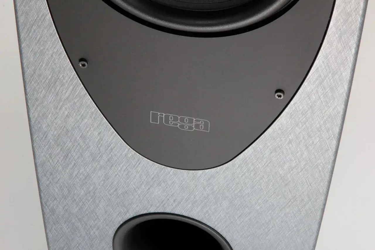 Gros plan sur une enceinte Rega, avec son logo grav&eacute; et une finition textur&eacute;e argent&eacute;e.