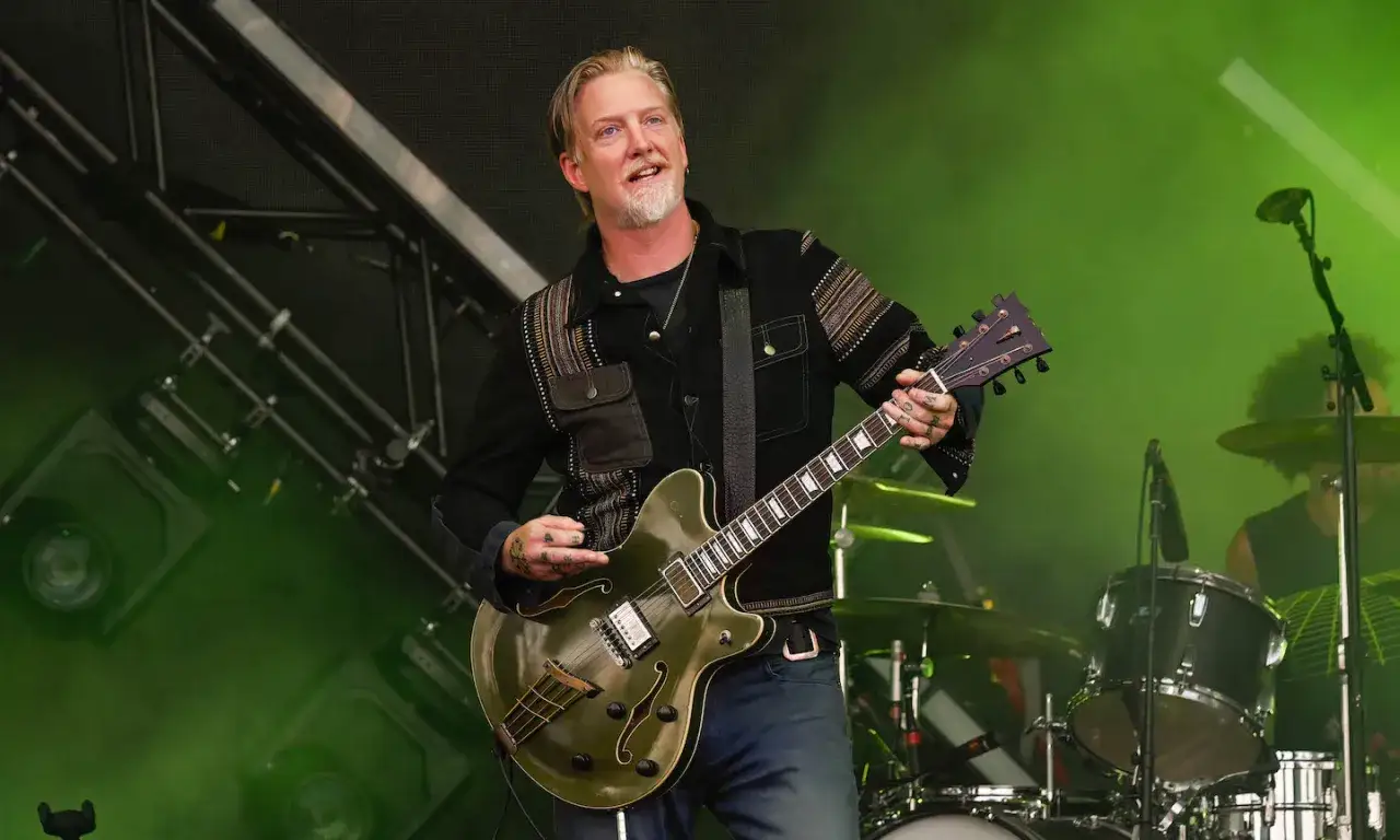 Josh Homme, un des membres de Queens of the Stone Age, joue de la guitare sur scène, éclairé par des lumières vertes.