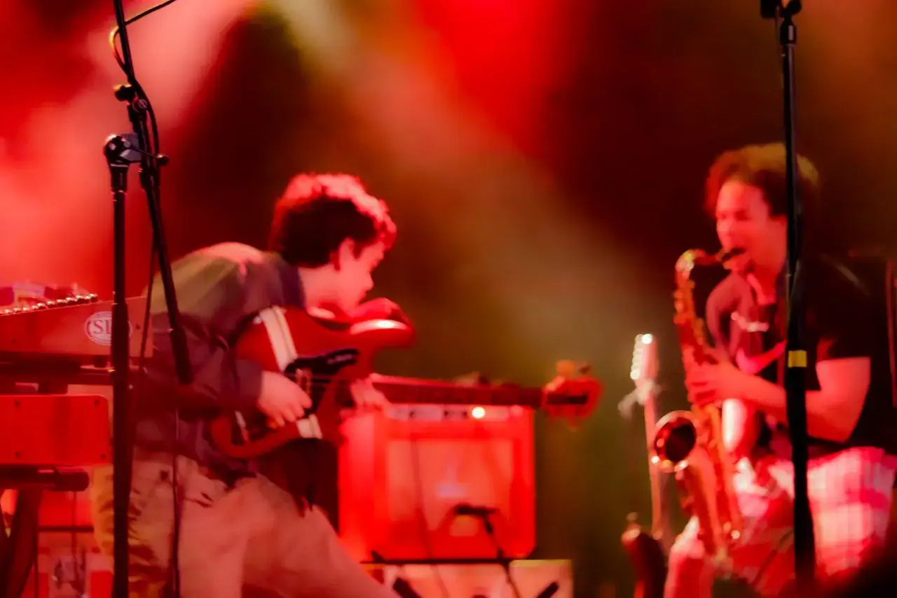 Un groupe de musique, black midi, joue sur sc&egrave;ne sous des lumi&egrave;res rouges. Un guitariste et un saxophoniste sont visibles.