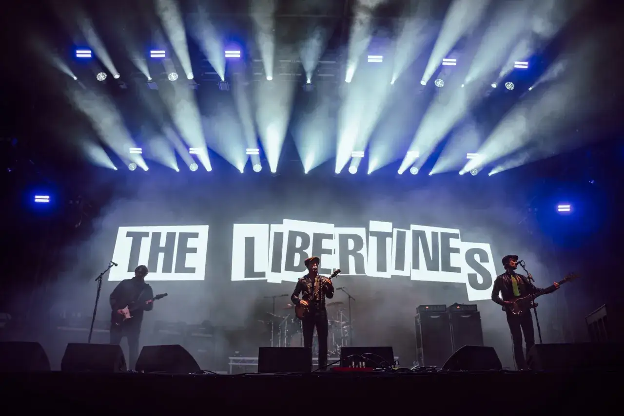 Sc&egrave;ne &eacute;clair&eacute;e par des projecteurs bleus, le groupe The Libertines joue devant une foule.