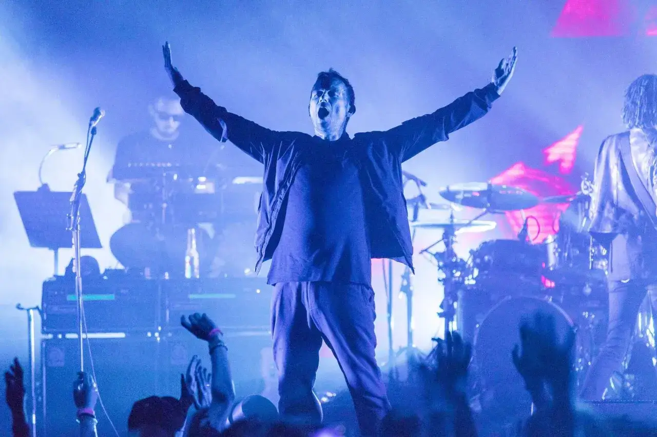 Damon Albarn, le chanteur, bras levés, en pleine performance avec son groupe. La foule en délire.