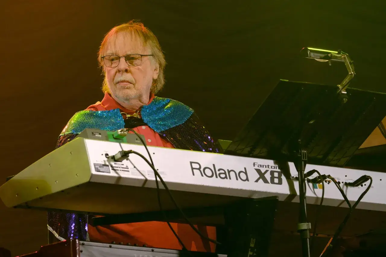 Un musicien du groupe Kean, portant une cape à paillettes bleues et vertes, joue du clavier Roland Fantom X8 sur scène.