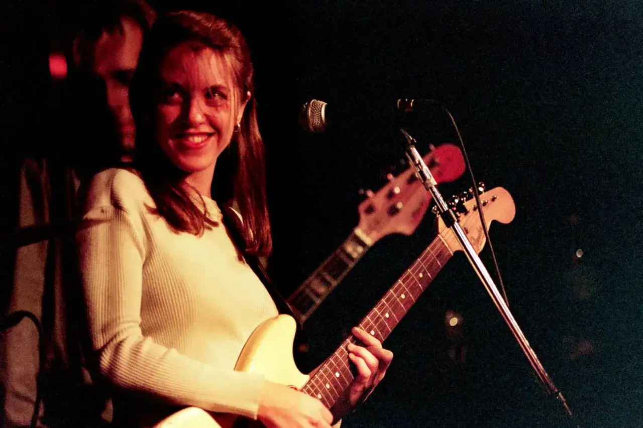 Liz Phair souriante, guitare à la main, sur scène.