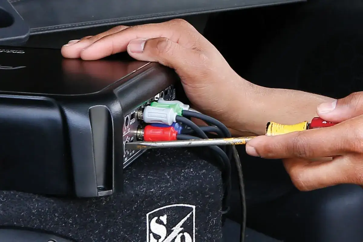 Main d'une personne branchant des c&acirc;bles RCA sur un amplificateur pour savoir si un caisson de basse fonctionne.