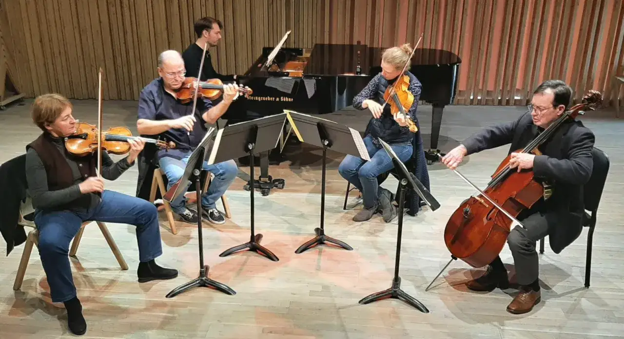 Un quatuor à cordes et un pianiste se préparent à jouer. Ils semblent trouver des musiciens pour un concert.