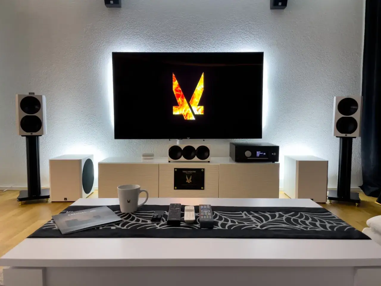 Système audio home cinéma avec caisson de basse blanc, enceintes sur pieds et TV. Réglage caisson de basse pour une immersion sonore parfaite.
