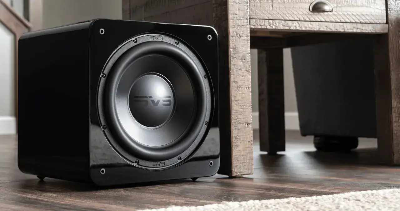 Un caisson de basse noir brillant SVS est placé près d'un meuble en bois rustique, optimisant le placement caisson de basse pour un son immersif.