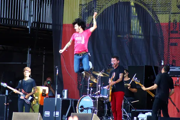 Un chanteur saute sur scène, micro en main, lors d'un concert en plein air. Le groupe joue avec énergie, une ambiance de festival.