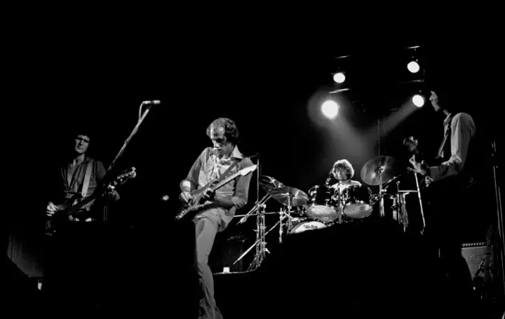 Quatre musiciens sur scène, guitares et batterie. Un aperçu de la **dire straits discography** en live.