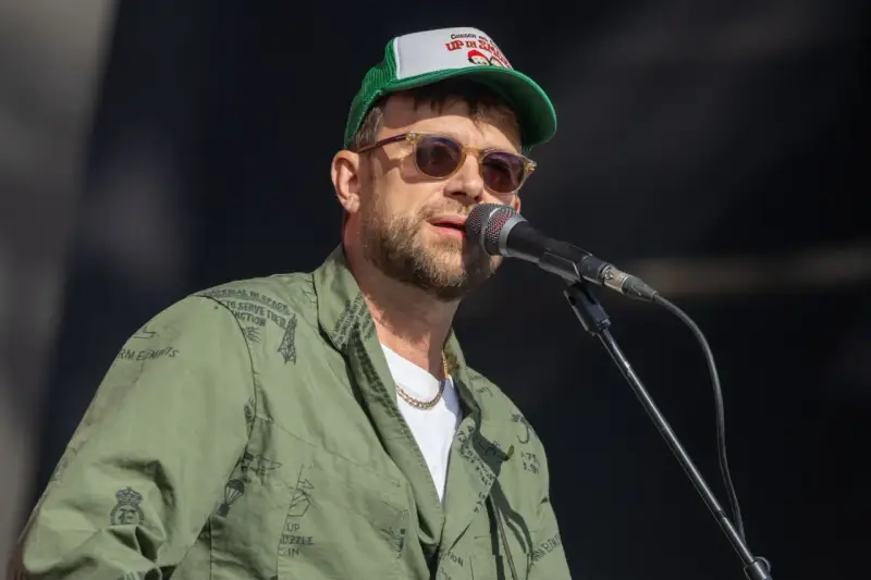 Damon Albarn, chanteur du groupe Gorillaz, porte une casquette et une veste verte ornée de motifs.